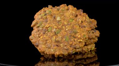 Stüdyo ışıklarının altında karanlık bir arkaplan karşısında parlak siyah yansıtıcı yüzeyde yavaşça dönen çikolata parçalı kurabiye yığınının sinematik görüntüsü..