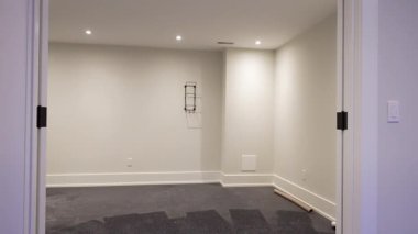 Tarafsız duvarlar, tentelenmiş tavan aydınlatması ve kurulum altında koyu zeminin bulunduğu yeni restore edilmiş bir konutta temiz ve minimal boş bir oda. Burlington, Kanada - 22 Nisan 2025.