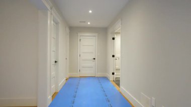 Temiz ve yeni yenilenmiş, beyaz duvarlı bir mesken koridoru, modern süsleme detayları, aralıklı tavan aydınlatması ve bitişik odalara açılan birden fazla kapı. Burlington, Kanada - 22 Nisan 2025.