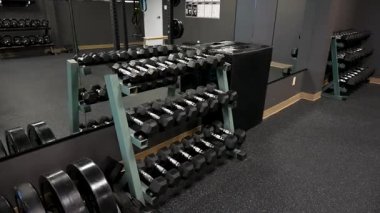 Multiple tiers of hexagonal dumbbells neatly arranged on metal rack inside contemporary studio gym with full wall mirror reflecting additional weights and functional training equipment. Burlington, Canada - April 22, 2025.