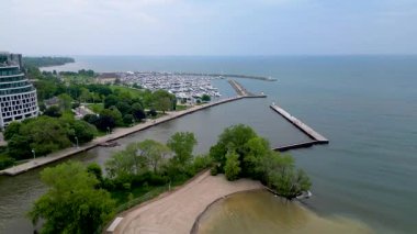 Drone perspektifi kumlu Bronte Sahili sahil şeridini, Ontario Gölü 'nün sakin sığ sularını, uzun beton iskeleli marina girişini, rıhtım girişini, yemyeşil parkları ve Oakville göl kıyısı boyunca yerleşim yerlerini yakalıyor. Temmuz, 27, 2025