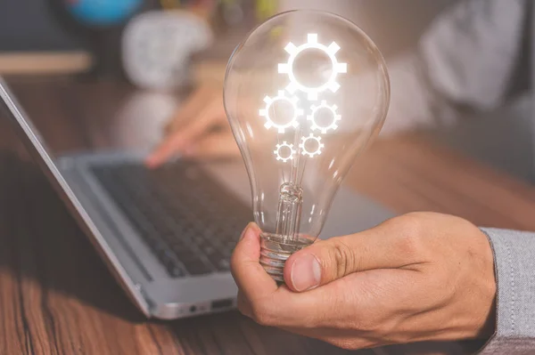 A man holding a light bulb gear symbol while using a computer