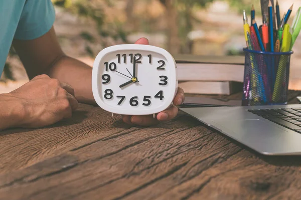 The hand holding the clock is at the work desk.