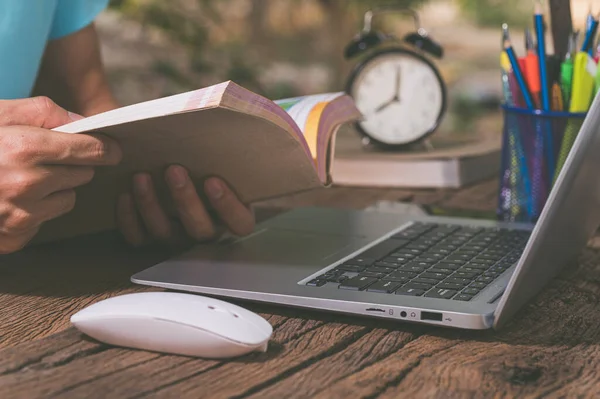 A person reading a book in front of a computer