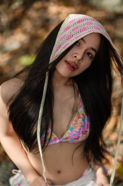 Kapüşonlu renkli bikinili genç bir kadın kumsalda güneşli bir günün tadını çıkarıyor. Enerjik atmosfer ve doğal güzellik onu mükemmel bir seyahat anı yapıyor..