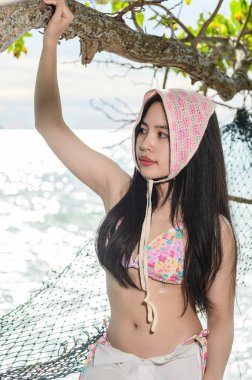 Renkli bikinili genç bir kadın kumsalda güneşli bir günün tadını çıkarıyor, doğayla iç içe. Neşeli duruşu yazın ve dinlenmenin özünü yansıtıyor..