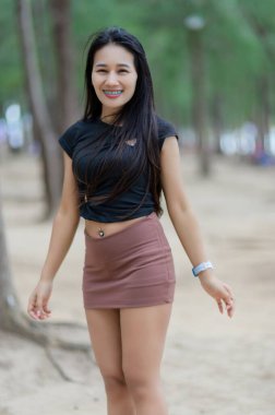 Kumsalın yakınındaki bir çam ormanında siyah gömlek ve kahverengi etek giymiş neşeli bir kadın duruyor. Onun parlak gülümsemesi yaz tatilinin özünü yakalar..