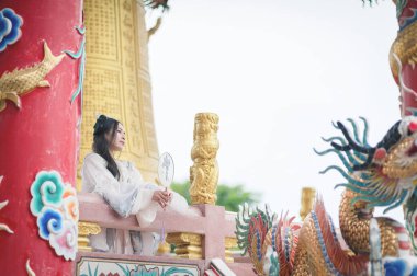 Güzel bir Hanfu kıyafeti giymiş genç bir kadın geleneksel Çin kültürünün zarafetini sergiliyor. Canlı bir tapınakta zarifçe oturuyor, dinginliği ve mirası somutlaştırıyor..