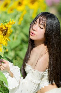 Güzel bir kadın, canlı bir ayçiçeği tarlasında güneşli bir bahar gününün tadını çıkarır. Doğanın güzelliğinin ve açan çiçeklerin neşesinin özünü yansıtır..