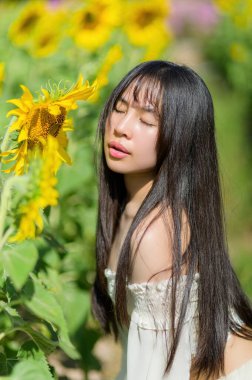 Güzel bir kadın ayçiçeği tarlasında zarifçe poz verir, baharın sıcaklığını ve neşesini kucaklar. Canlı renkler huzurlu ve büyüleyici bir atmosfer yaratıyor..