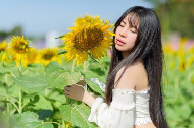 Güzel bir kadın, canlı bir ayçiçeği tarlasında güneşli bir bahar gününün tadını çıkarır. Doğanın cazibesi onun sakin ifadesiyle harmanlanır ve bir neşe anı yakalar..