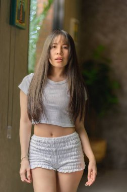 Genç bir kadın, modern bir iç mekan içinde şık bir günlük kıyafete olan güvenini sergiliyor. Doğal ışık, ifadesini ve saçlarını güçlendiriyor ve sakin bir atmosfer yaratıyor..