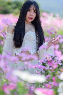 Işıl ışıl bir kadın çiçek tarlasının ortasında zarif bir şekilde poz veriyor. Baharın canlı renkleri büyüleyici bir zemin oluşturur, güzelliğini ön plana çıkarır..