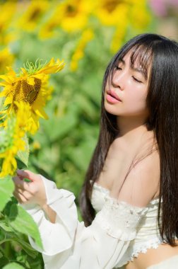 Güzel bir kadın, bahar boyunca canlı bir ayçiçeği tarlasında güneşli bir günün tadını çıkarır. Neşeli ifadesi ve canlı çiçekleri huzurlu ve uyumlu bir atmosfer yaratıyor..