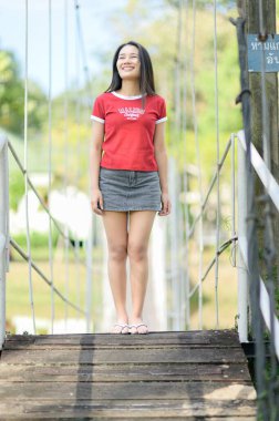 Neşeli genç bir kız güvenli bir şekilde kırsal ahşap bir köprüde duruyor. Parlak güneş ışığı altında mutluluk saçıyor. Huzurlu doğayla çevrili..