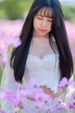 Güzel bir kadın, bir bahar tarlasında canlı pembe çiçeklerin arasında zarif bir şekilde duruyor. Huzur ve cazibe saçıyor. Yumuşak güneş ışığı onun huzurlu ifadesini güçlendirir, doğal güzelliğin bir anını yakalar..