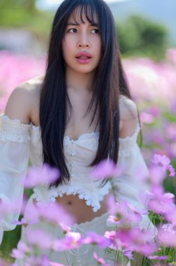 Göz kamaştırıcı bir kadın renkli çiçeklerle dolu canlı bir bahar tarlasında duruyor. Çiçek açan güzellik ve zarafet çiçek açan doğanın ortasında. Huzur ve neşeyi somutlaştırıyor..