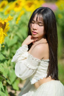 Güzel bir kadın, canlı bir ayçiçeği tarlasında baharın sıcağını kucaklıyor. Onun dingin ifadesi ve dalgalı saçları çiçek açan manzaranın neşeli atmosferini tamamlıyor..