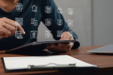 Bir kişi, teknoloji simgelerini gösteren bir tabletle etkileşime girer, profesyonel bir çalışma ortamında dijital yenilikleri ve modern iletişimi sembolize eder.