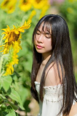 Güzel bir kadın çiçek açan ayçiçeklerinin arasında zarifçe poz verir, baharın özünü yakalar. Güneş ışığı onun dingin ifadesini vurgular, doğanın canlı renklerini gözler önüne serer.
