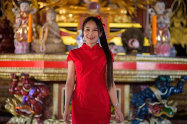 Neşeli bir kadın canlı kırmızı geleneksel bir elbiseyle duruyor, güzel dekore edilmiş bir tapınakta yeni yıl şenliklerini kutluyor. Sahne mutluluk ve kültürel önem taşıyor..