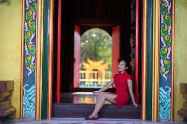 Canlı kırmızı geleneksel elbiseli genç bir kadın zarif bir şekilde renkli bir kapı eşiğinde oturuyor, neşe ve kültürle dolu yeni yıl kutlamalarının özünü somutlaştırıyor..