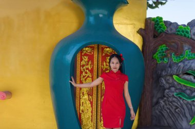 Geleneksel kırmızı elbiseli genç bir kadın canlı bir girişte duruyor, neşeli tavırları ve şenlikli kıyafetleriyle yeni yıl kutlamalarının özünü yakalıyor..