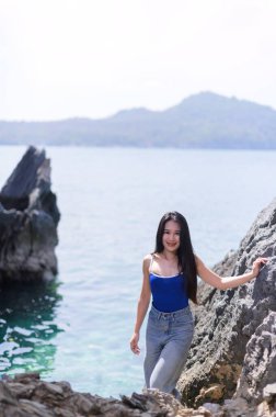 Genç bir kadın, sakin turkuaz sularla çevrili kayalık bir sahilde poz veriyor. Görüntü, doğanın güzelliğini gösteren Koh Si Chang 'de mükemmel bir tatilin özünü yansıtıyor..