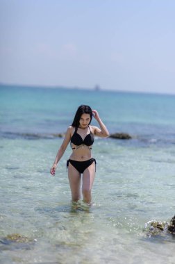 Koh Si Chang, Chonburi 'de yaz tatilinin huzur veren güzelliğini görün. Bir kız berrak sularda yürüyor, kumsalda güneşli bir günün tadını çıkarıyor..