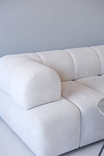 Stylish white sofa features rounded shapes and soft fabric, positioned against a sleek gray wall, enhancing modern living space ambiance and comfort