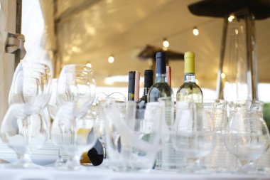 Cam eşyalar ve şarap şişeleri çadırın altında temiz bardaklar, sürahiler ve dışarıdaki tabaklar dahil olmak üzere sicim lambalarıyla düzenlenir.