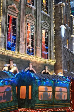 Canlı ışıklarla süslenmiş şenlikli tren çarpıcı bir şekilde aydınlatılmış bir binanın önüne yerleştiriliyor. Bu da tatil kutlamaları için mükemmel bir kış ortamı yaratıyor.