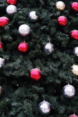 Parlak kırmızı, gümüş ve altın süslerle süslenmiş Noel ağacı, Noel neşesi ve yeni yıl kutlamaları için sıcaklıkla dolu bir şenlik ortamı yaratıyor.