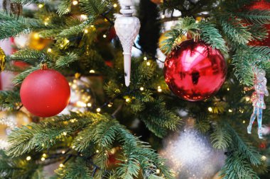 Vibrant red and silver ornaments adorn a Christmas tree, nestled among lush green branches and sparkling lights, evoking a warm holiday spirit