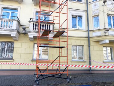 Bir konut binasının onarımı için yapı iskelesi kuruldu, güvenlik bariyerleri yerleştirildi, kentsel bakım ve inşaat faaliyetleri vurgulandı