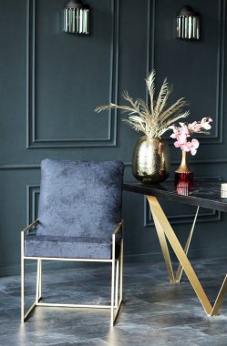 Şık, koyu renk iç dekoratif vazolara sahip modern bir masanın yanında altın bacaklı lüks bir donanma koltuğu ve atmosferi güçlendiren zarif çiçek düzenlemeleri sergiliyor.