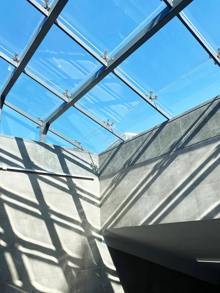 Güneş ışığının cam tavandan süzülen, gri duvarlarda çarpıcı geometrik gölgeler yaratan, modern mimari tasarım ve ambiyansı vurgulayan...