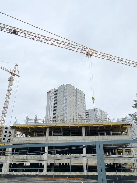 İnşaat alanı, bulutlu bir gökyüzünün altında inşaat iskelesi olan vinçleri ve bitmemiş konut binalarını gösteriyor, kentsel gelişimi ve altyapı ilerlemesini vurguluyor