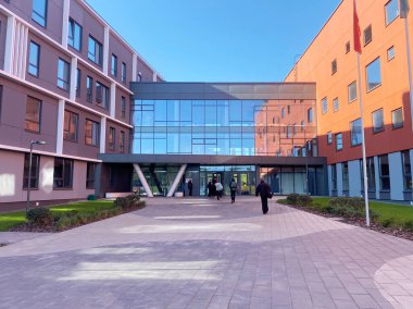 Modern okul binasında peyzajlı yolları ve renkli cepheleri olan geniş camdan bir giriş, öğrenciler ve ziyaretçiler için davetkar bir atmosfer yaratıyor.