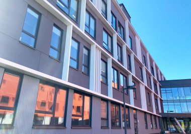 Geniş pencereli ve malzemelerin karışımlı modern eğitim tesisi, parlak mavi gökyüzü altında çağdaş tasarım unsurları sergiliyor