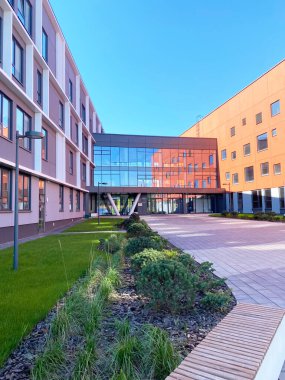 Modern okul binasında, güneşli hava koşulları altında canlı dış duvarlarla çevrili büyük cam bir girişi ve manzaralı bir avlusu vardır.