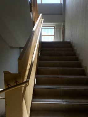 Güneş ışığı, bej kiremitler ve ahşap korkuluklar ile merdiven üzerinde karmaşık gölgeler yaratır. Bu da bizi çağdaş bir iç mekanda parlak bir pencereye götürür.