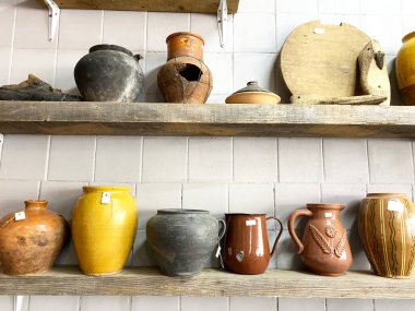 Antika bir mağazadaki ahşap raflarda sergilenen antika çömlek koleksiyonu, seramik kap ve dekoratif eşyaların çeşitli şekillerini ve renklerini vurguluyor
