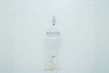 Tuvaletteki fayanslı bir duvara yerleştirilmiş beyaz pisuar, temiz estetik kapakçık ve basit, çağdaş bir tasarım sergiliyor.