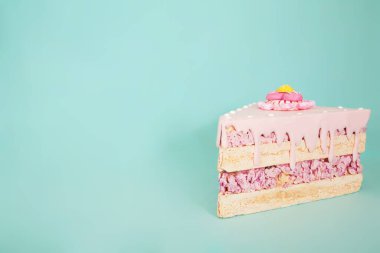 Pembe şekerli ve dekoratif kremalı bir dilim pasta pastel mavisi arka planda oturur, sünger ve krema katmanlarını renklendirir.