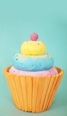 Yapay kek polistiren köpükten yapılmıştır. Üzerinde pembe top bulunan canlı mavi, sarı ve pembe katmanlar açık mavi bir zemin üzerine dizilmiştir.