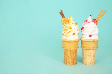 Renkli suni köpük şekerler iki dondurma külahında turkuaz arka planda sergilenerek yaratıcı tasarım elementleri için geniş bir kopya alanı sağlıyor.