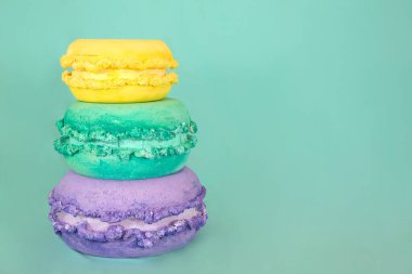 Birbiri üzerine dizilmiş üç sarı, yeşil ve mor badem kurabiyesi. Nane yeşili arka planda geniş kopya alanı var.