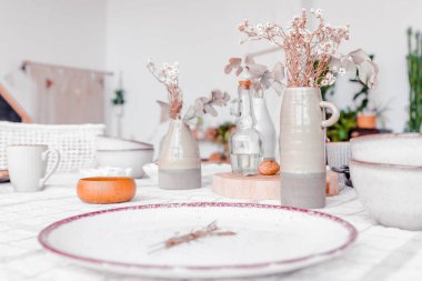 Kurumuş çiçekleri, cam şişeleri ve kırsal bulaşık takımlarını tutan seramik vazolarla güzelce düzenlenmiş masa, yemek deneyimleri için samimi atmosferi artırıyor.