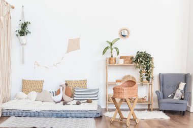 Bohemlerden esinlenilmiş iç mekan, desenli yastıkları olan rahat bir oturma alanı, yeşillikli ahşap bir raf ve parlak bir alanda hasır bir beşik.